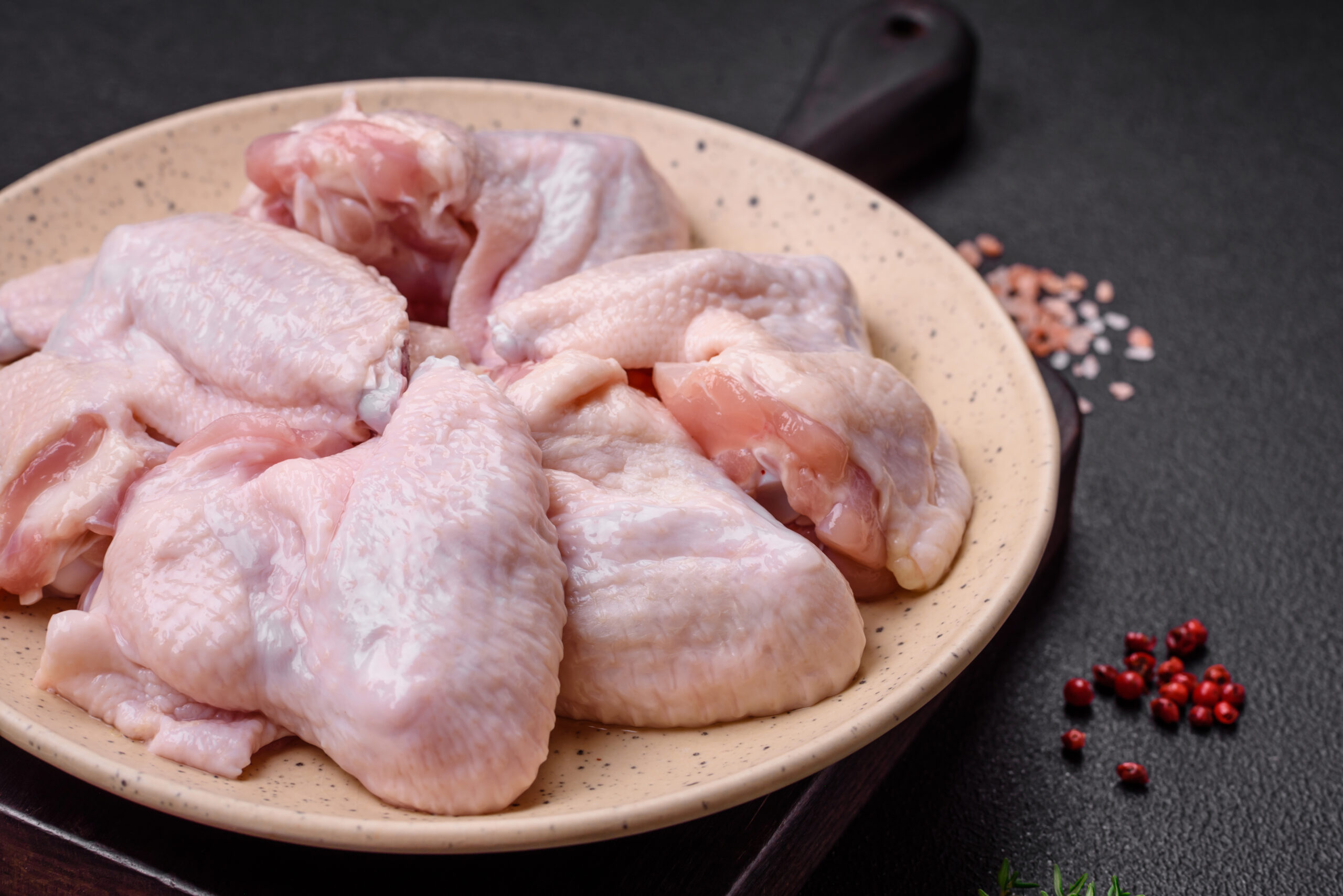 Fresh raw chicken wings with salt and spices prepared for baking on a dark concrete background