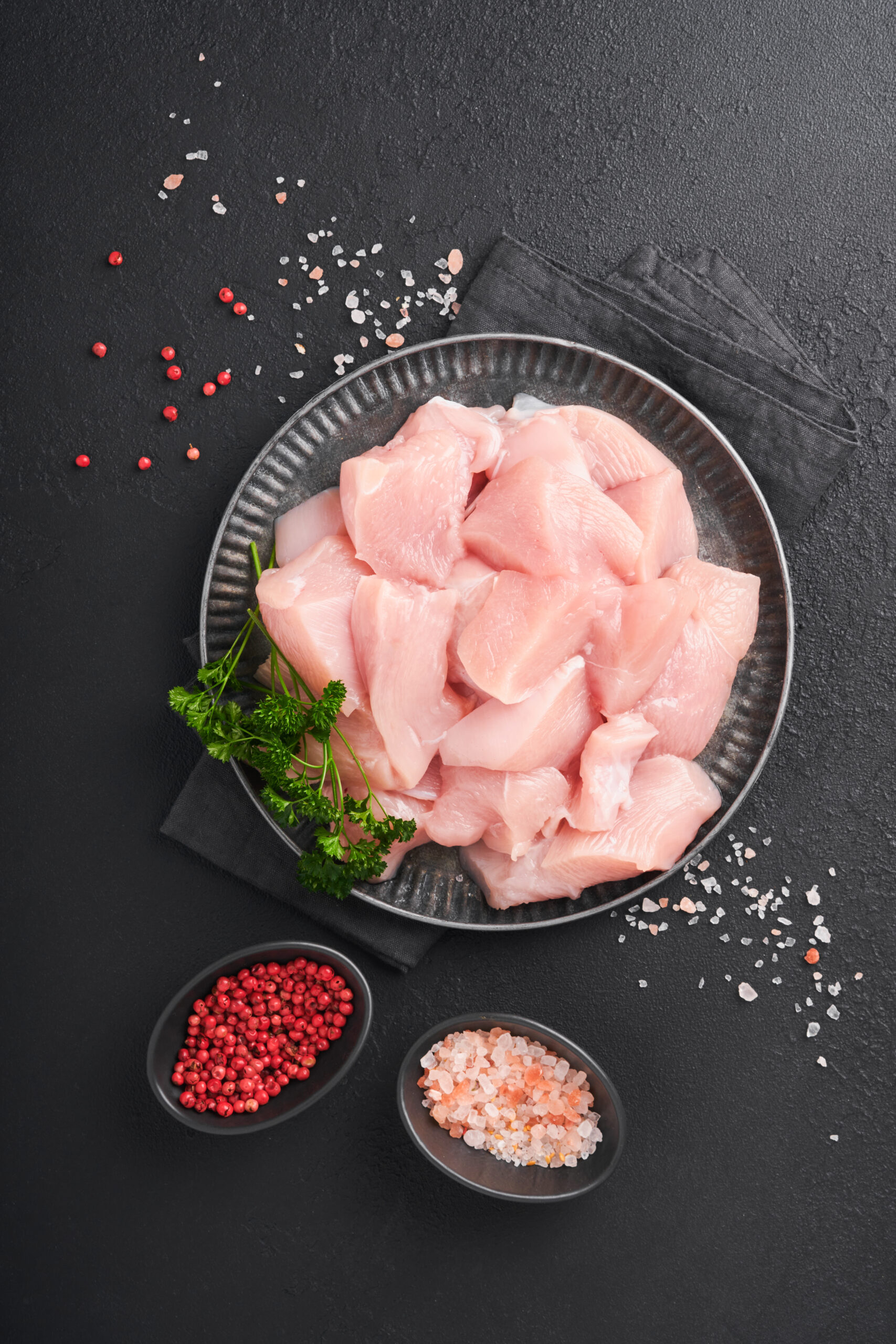 Raw chicken breast sliced or cut pieces on wooden cutting board with herbs and spices on dark slate, stone, concrete background. Raw chicken meat. Top view with copy space. Mock up.