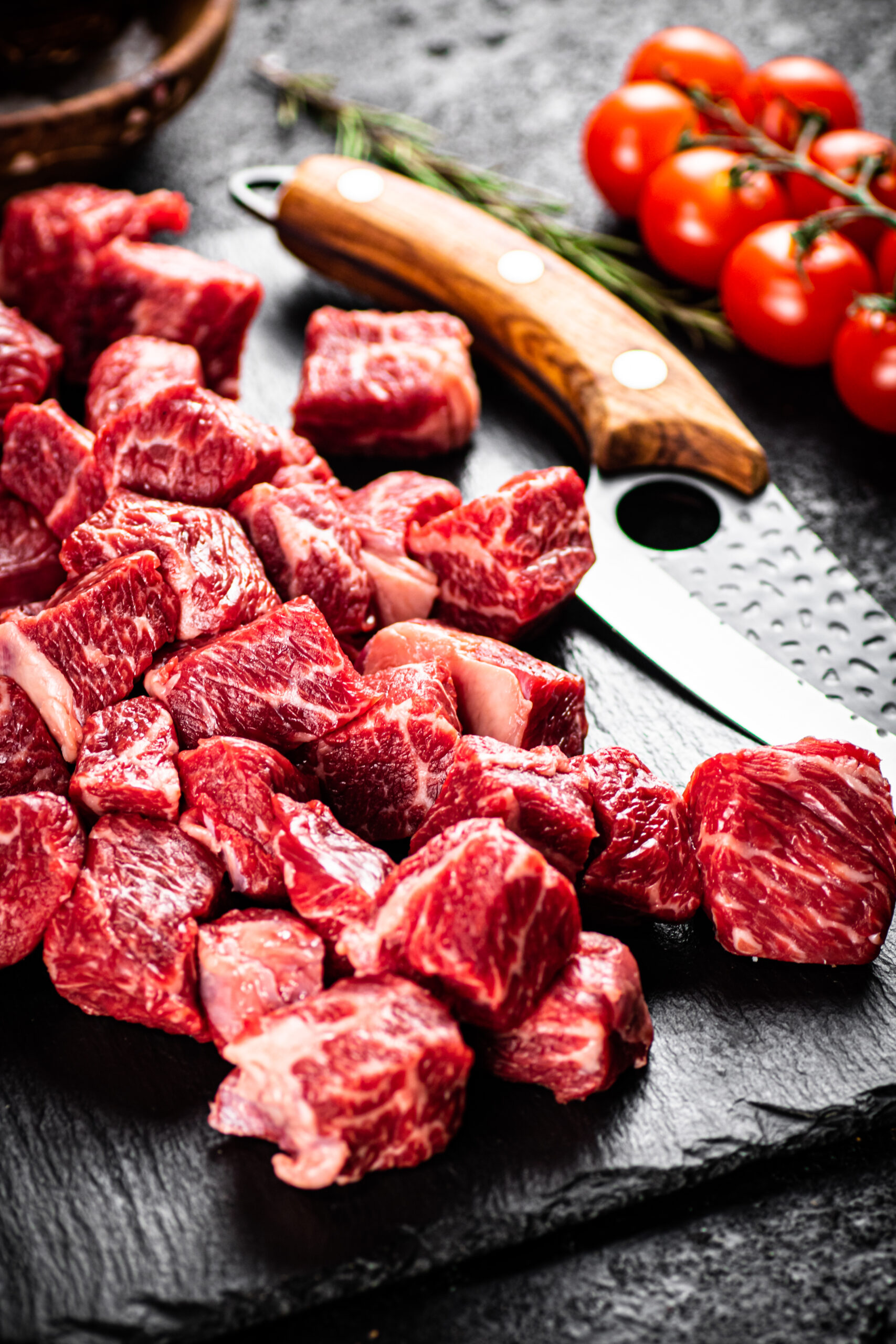 Raw pieces of beef on a stone board with a sprig of rosemary and a knife. On a black background. High quality photo